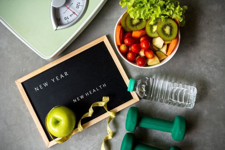 New Year's resolution sign with a scale, weights, fruit and a water bottle
